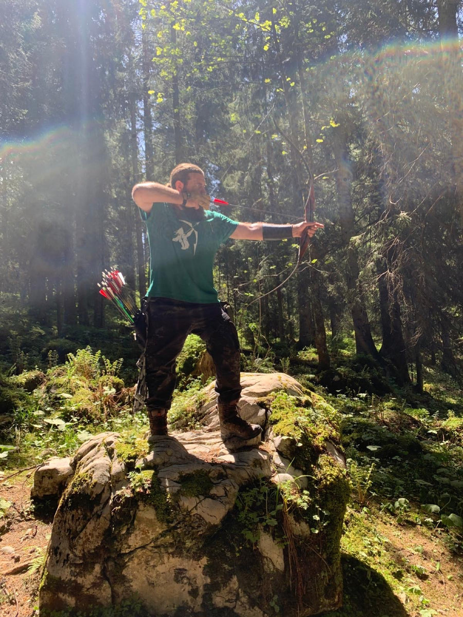 Bogenschütze mit Recurvebogen auf einem Felsen im Wald